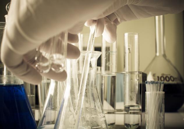 Photo: a gloved hand reaching for laboratory test tubes and flasks