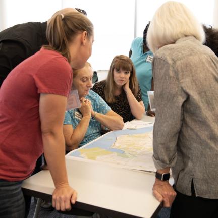 Photo: a group of individuals looking at a map on a table.