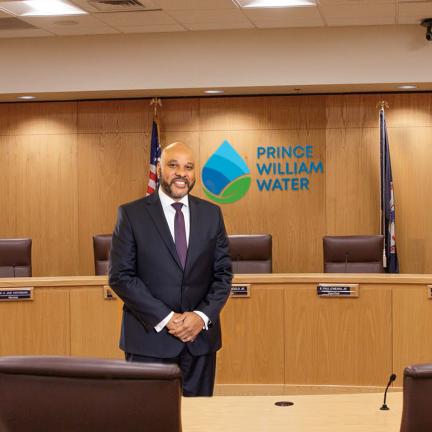 Photo: a man in a suit in a boardroom with a water drop logo on the wall