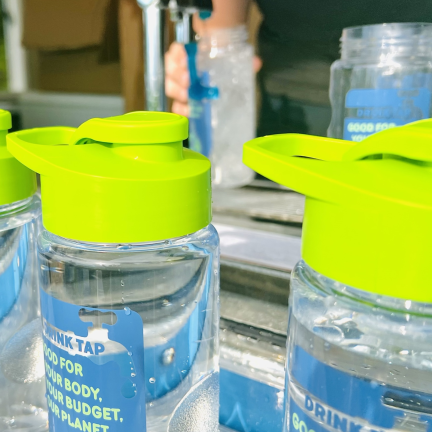 Photo: reusable water bottles. someone is filling one from a tap in the background.