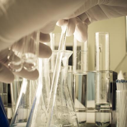 Photo: a gloved hand reaching for laboratory test tubes and flasks