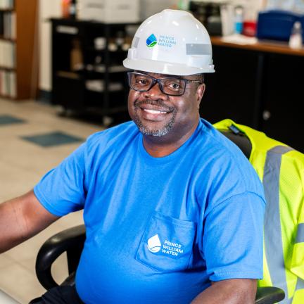 A man in a hard hat sitting at a computer smiling.