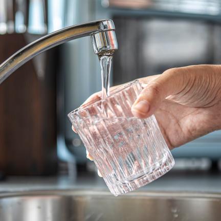 A hand filling a glass of water from a kitchen sink tap
