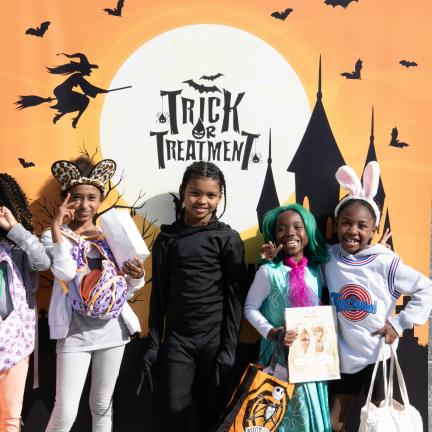 Children gather in Halloween costumes in front of a spooky banner that reads "Trick or Treatment"