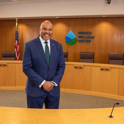 Prince William Water General Manager Calvin Farr standing in a suit in a board room with the Prince William Water logo on the wall