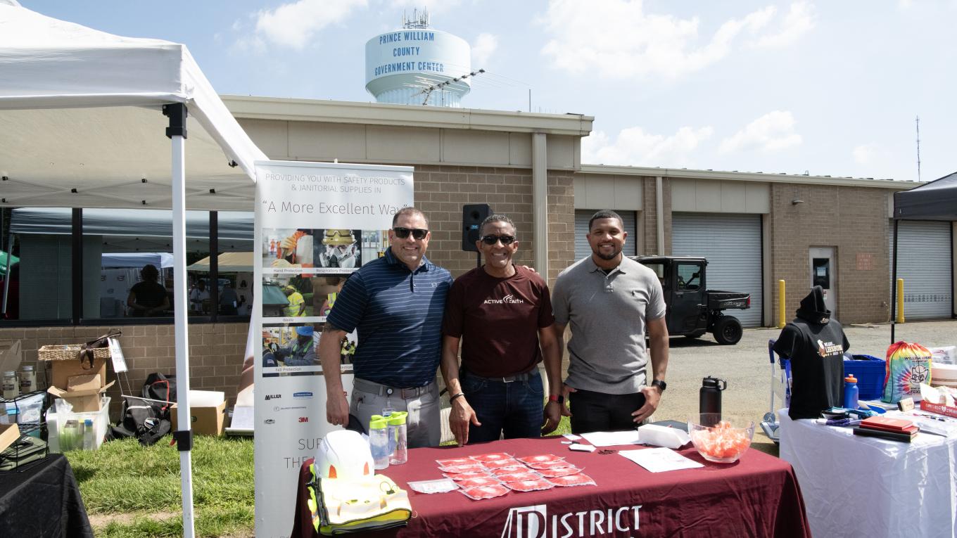 Photo: three individuals standing at a table with products on display