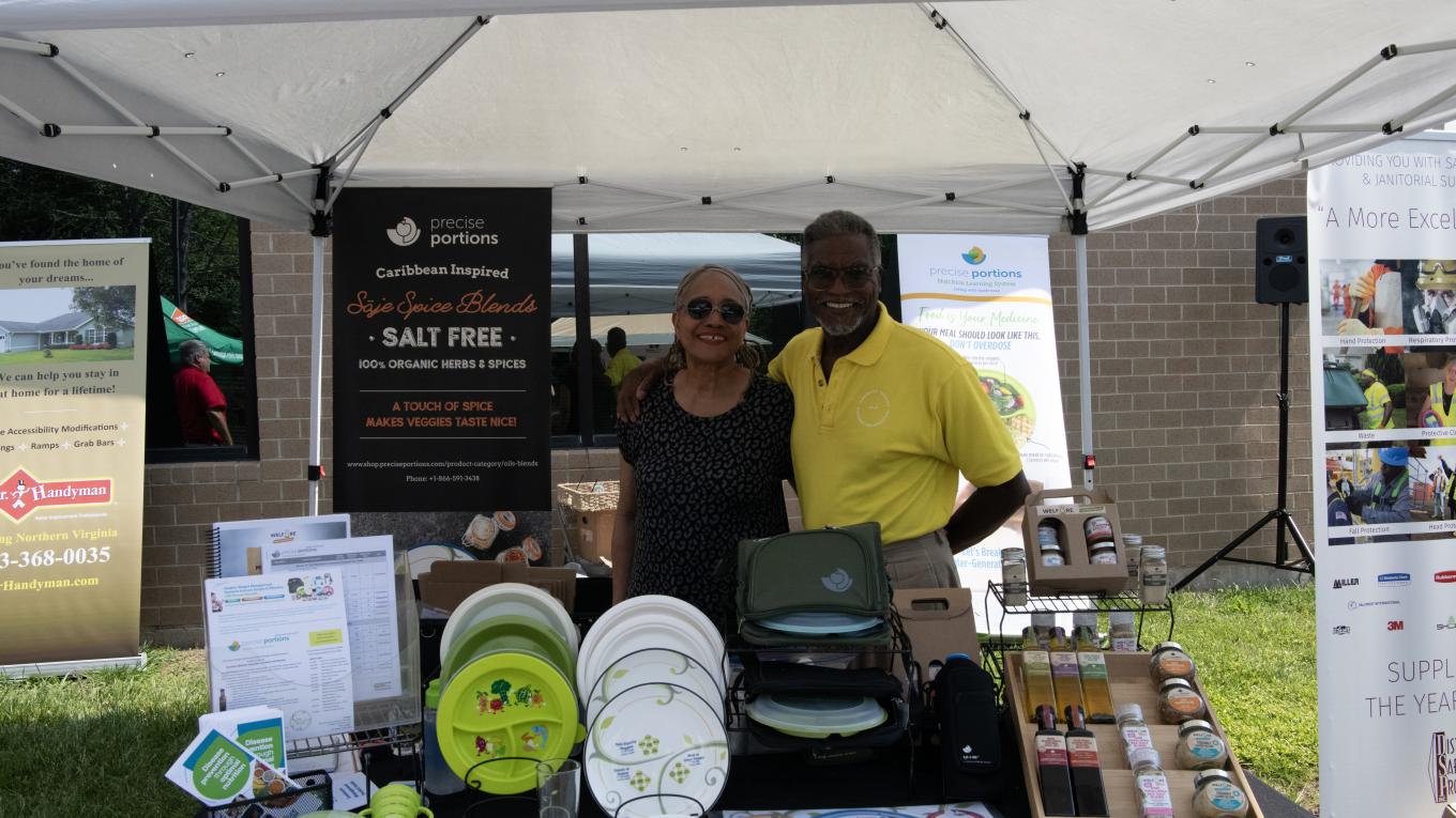 Photo: individuals standing at a table under a canopy with products on display