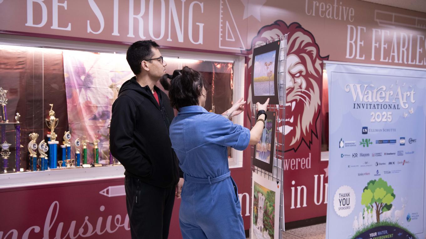 Two individuals looking at artwork on a panel. A mural is painted on the wall in the background.