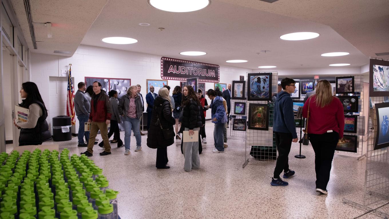 Individuals viewing an art gallery in a high school lobby
