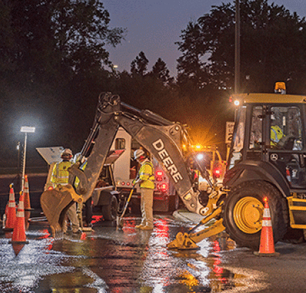 A group of utility workers uses heavy equipment to fix a nighttime water main break