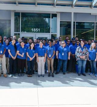 Photo: a group of individuals in blue shirts standing in front of a building