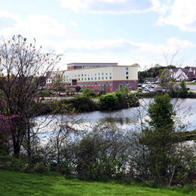 A multi-story concrete building stands near a lake during springtime