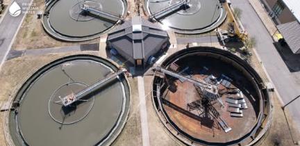A bird's-eye view of four round clarifiers at a wastewater treatment facility. One of the clarifiers is empty to have construction performed on it.