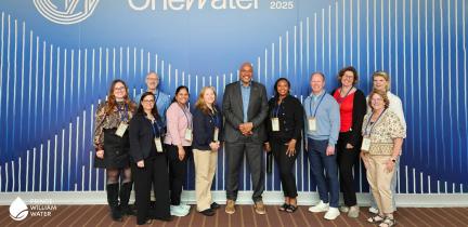 A group of people in business attire in front of a blue background that reads "One Water"