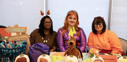 Individuals dressed in costumes sit at a Halloween-themed tabling event
