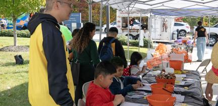 Individuals create Halloween-themed crafts under a tent at an event outdoors