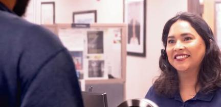 A smiling customer service representative greets a customer at the customer service window.