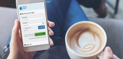 A top-down view of an individual's lap. They are holding a mobile phone in their left hand and a coffee in their right hand.