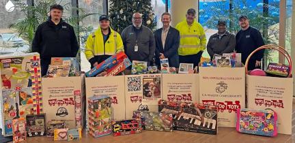 A group of utility employees standing behind full Toys for Tots boxes