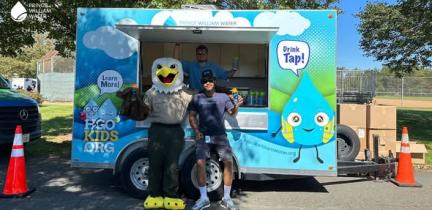 An individual and someone in a bald eagle costume standing in front of a blue and green concession trailer
