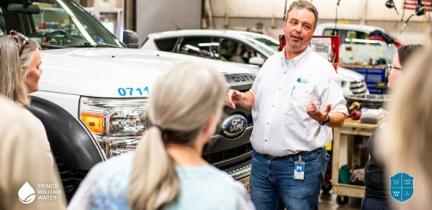 An adult gives a presentation in an auto-body shop to other adults.