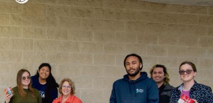 A group of employees standing in front of a large donation of non-perishable foods an drinks.