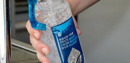 A hand filling a reusable water bottle at a tap