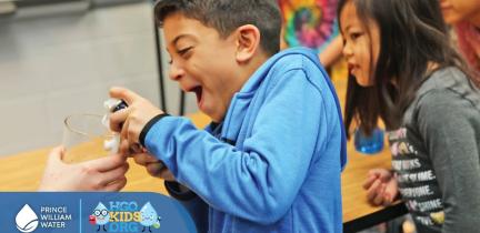 A young child laughing while spraying shaving gel into a glass vase for a science experiment