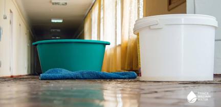 Plastic bins and towels collect water in a flooded indoor area.