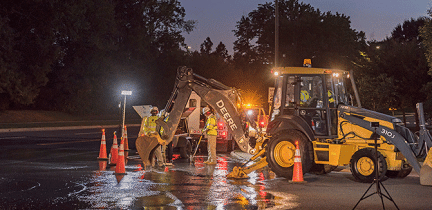 A group of utility workers uses heavy equipment to fix a nighttime water main break