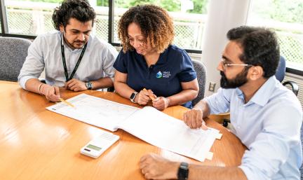 Photos: three individuals sit at a conference table looking at documents and a calculator.