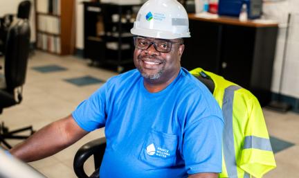 A man in a hard hat sitting at a computer smiling.