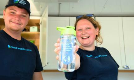 Photo: two young people in a concession trailer. One holds up a reusable water bottle and is smiling
