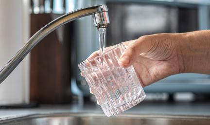 A hand filling a glass of water from a kitchen sink tap