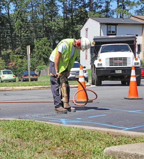 Photo: a utility worker in safety gear using a jackhammer to drill through pavement