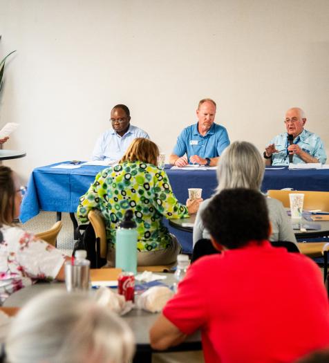 Photo: a crowd watches as individuals give a panel presentation