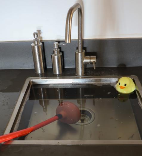 Photo: a kitchen sink overflowing. A plunger is in the sink.