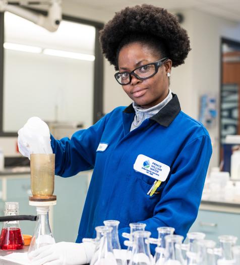 Photo: A woman in a lab coat performing testing on water in a laboratory setting